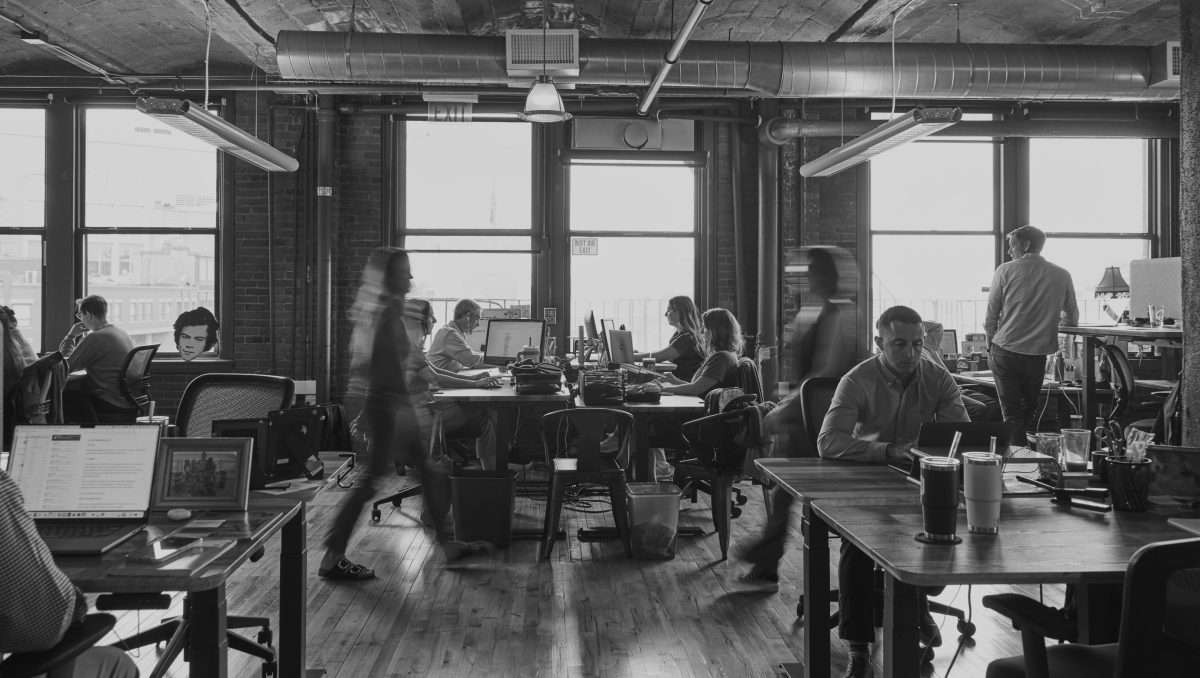 A black and white photo of the CTP office space, with employees some employees working alone at their desks while others chat in small groups.
